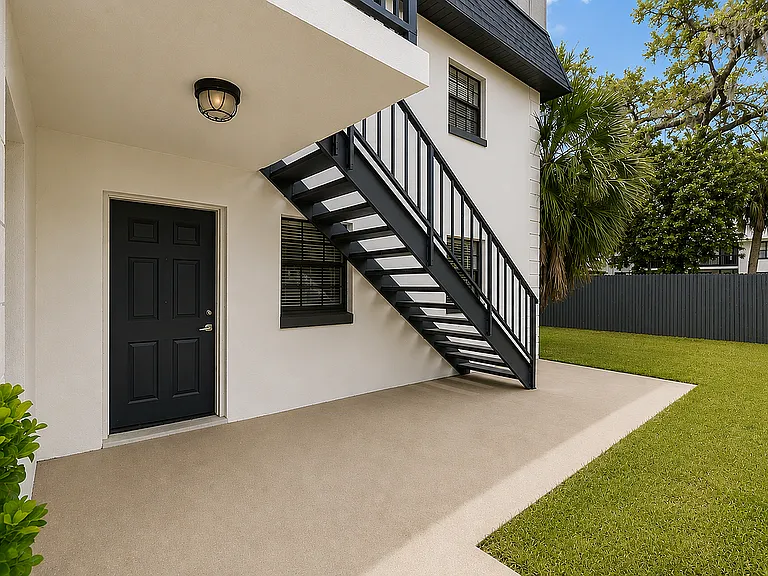 Inviting apartment entryway with sleek black stairs, elegant modern door, and spacious patio leading to a lush green lawn.