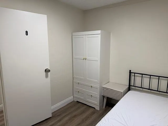 Furnished bedroom with a bed, nightstand, and wardrobe for convenient storage in a simple, low-maintenance layout. - Squires St