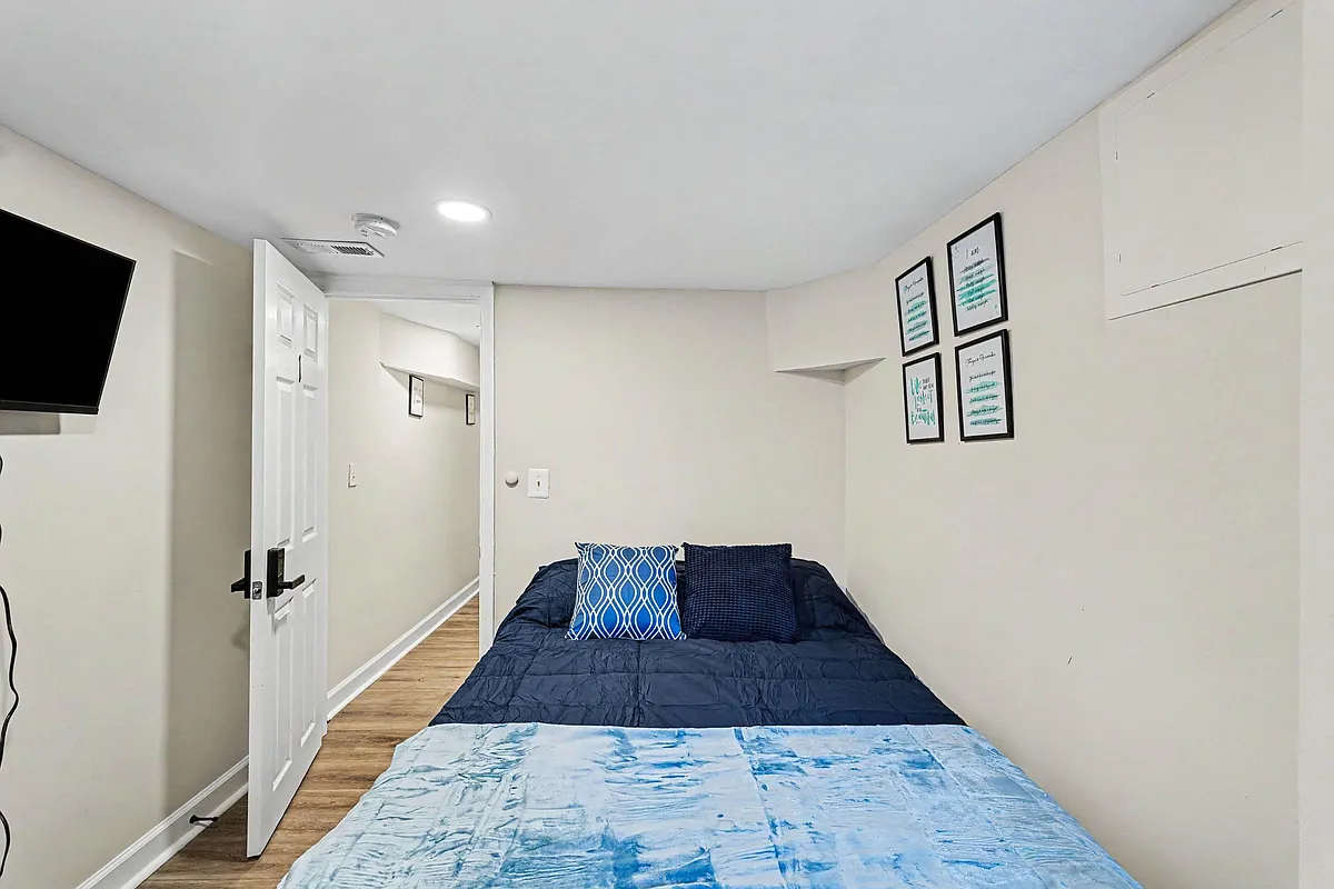Furnished bedroom with a full bed, wall-mounted TV, and easy access to the hallway in a clean, neutral-toned layout. - N Luzerne Ave