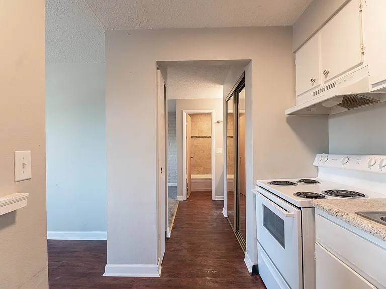Bright and inviting apartment hallway leading to a cozy bathroom, featuring gleaming hardwood floors and modern kitchen amenities with elegant white cabinetry.