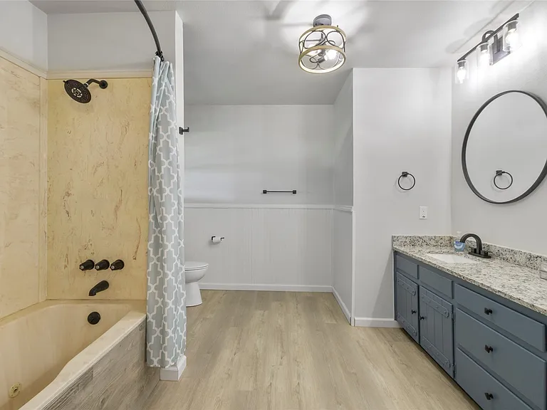 Spacious bathroom featuring a full tub and shower with stone-look surround and black fixtures