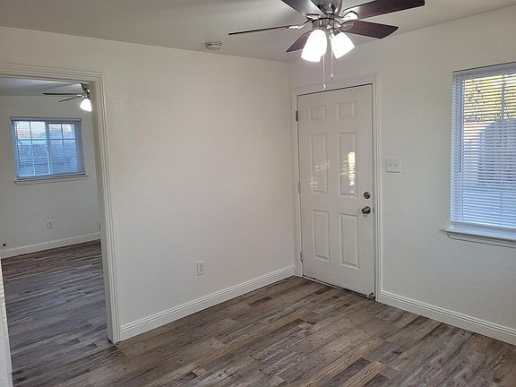 Living room with ceiling fan, showing front door and view into bedroom.