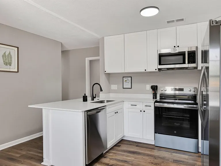Updated kitchen with white shaker cabinets, quartz-style counters, and stainless steel appliances with peninsula seating.