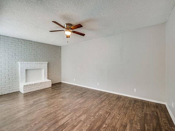 Unfurnished living room featuring a textured ceiling, brick wall, dark wood-style floors, and ceiling fan