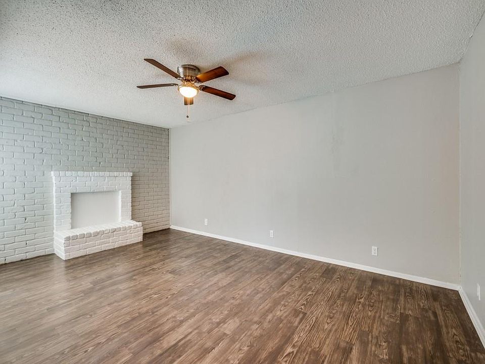 Unfurnished living room featuring a textured ceiling, brick wall, dark wood-style floors, and ceiling fan