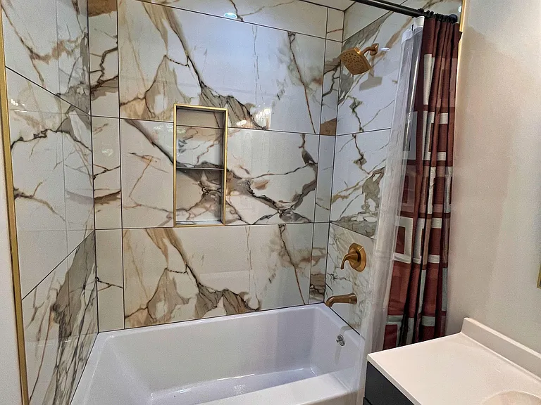Updated full bath with tiled tub/shower surround, built-in niche shelving, and a vanity with countertop space.