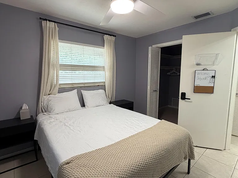Furnished bedroom with a ceiling fan, window with curtains, bedside tables, and an open closet for convenient storage.