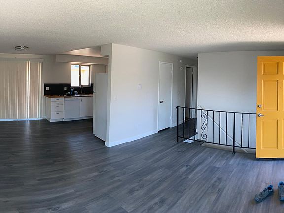Living room looking into kitchen. Hall to bathroom and two upstairs bedrooms. Stairs behind railing head down to basement.