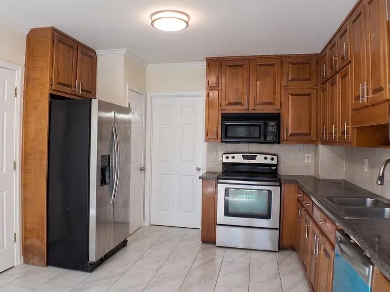 Galley-style kitchen with ample wood cabinetry, stainless steel appliances, tiled floors, and long counters for meal prep.