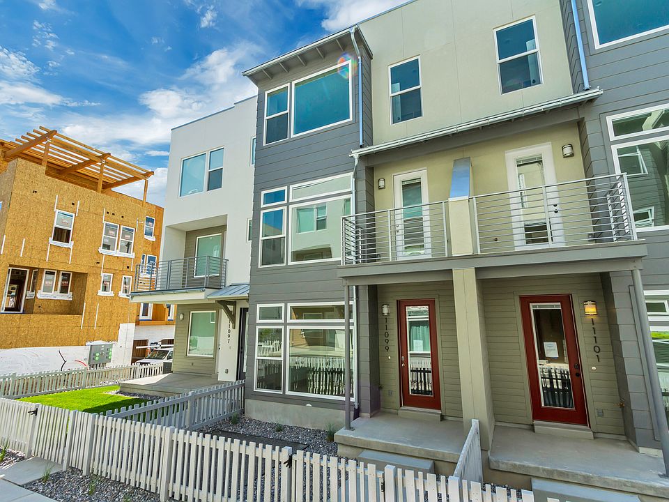 Modern townhouses with large windows, balconies, and small front yards enclosed by white picket fenc