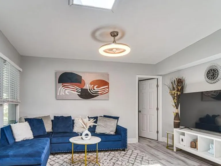 Living room with sectional seating, large TV setup, and a wide window bringing in natural light.