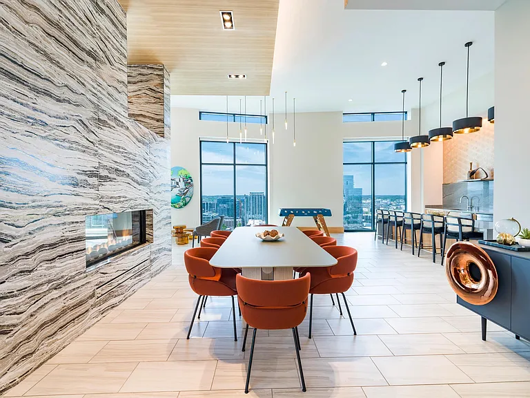 Community lounge with a shared table, fireplace, and bar seating framed by expansive windows and warm architectural details.