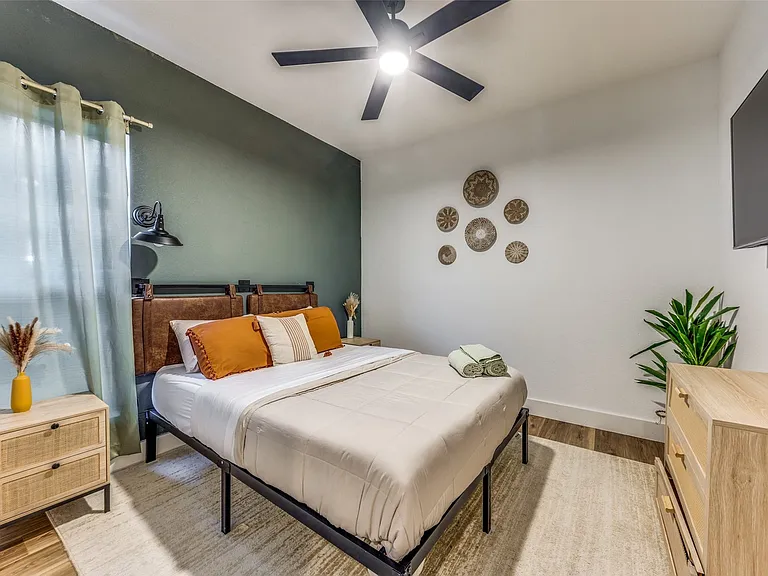 Bedroom featuring an accent wall, window with curtains, wood-finish flooring, ceiling fan with integrated lighting, and a wall-mounted television