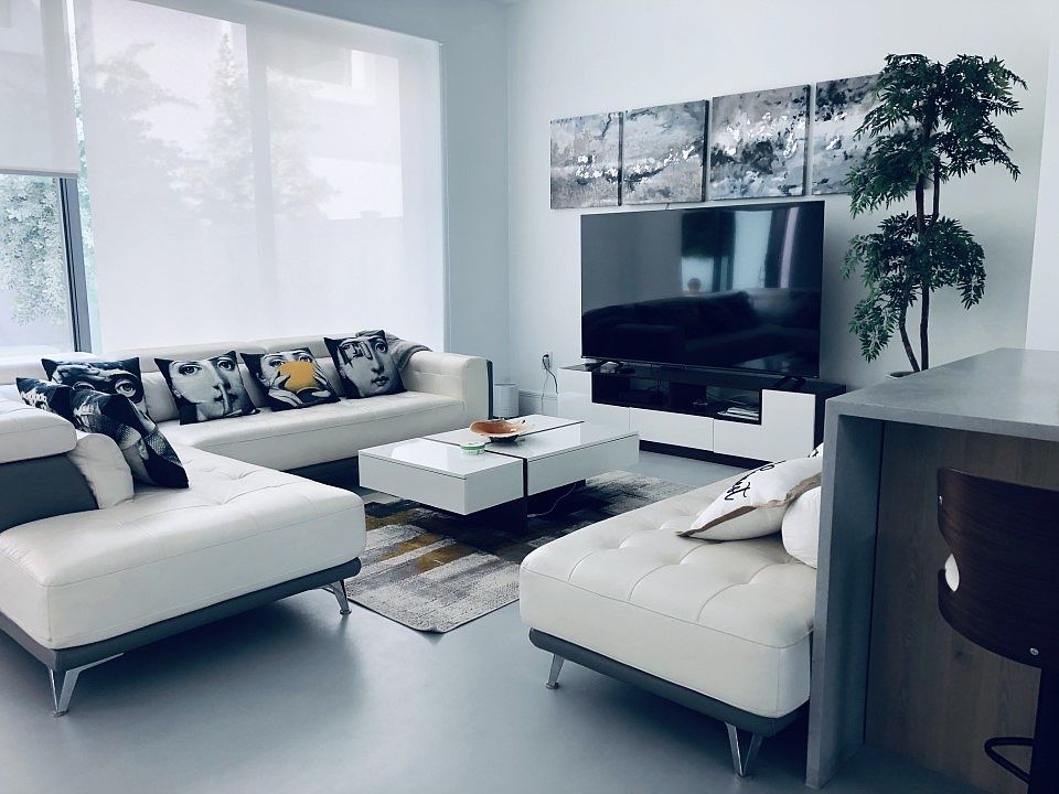 Living area features leather couches, a recliner, and a 75" smart TV. The floor-to-ceiling windows overlook the courtyard, making it an ideal spot for relaxing, entertaining, or unwinding. Perfect for both hosting guests and quiet evenings in.