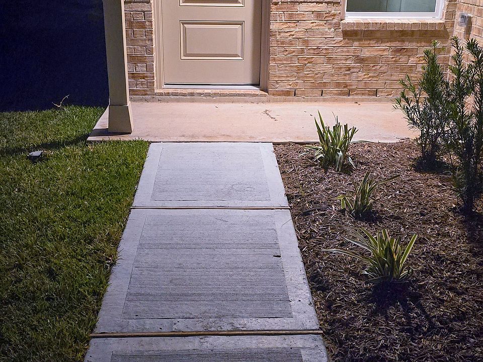 Well-lit front entry featuring a covered porch, brick exterior, and neatly landscaped walkway.