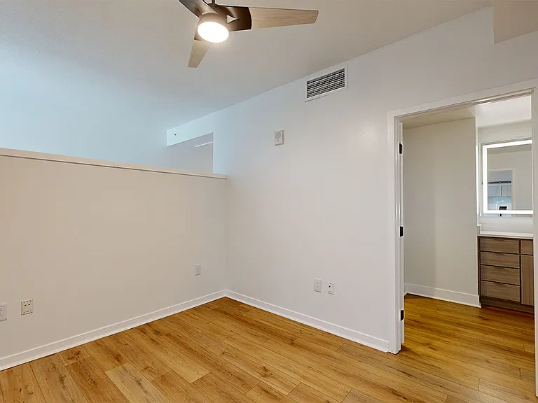 Spacious apartment bedroom with large closet, attached bathroom and wood-style flooring.