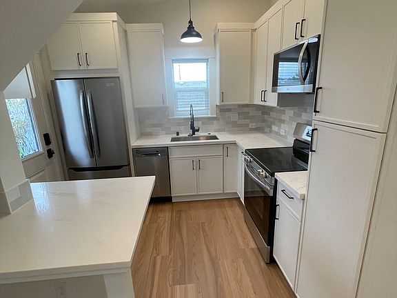 View into the kitchen from the living area. Full size refrigerator with icemaker, Dishwasher, sink with pull out faucet and garbage disposal, electric range/oven and microwave range/hood. Built in trash pull out in cabinets
