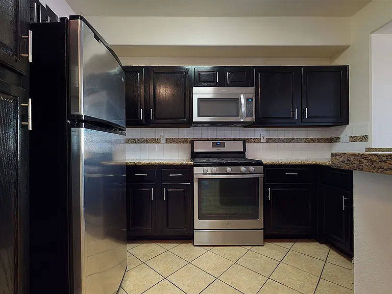 Apartment kitchen with stainless steel appliances, granite countertops and tile flooring.