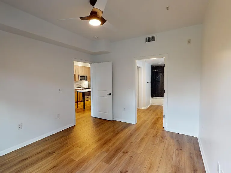 Spacious apartment bedroom with attached bathroom and wood-style flooring.