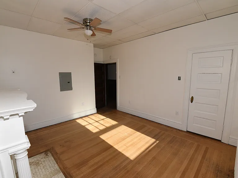 Spacious bedroom with original hardwood floors, abundant natural light, a ceiling fan, classic architectural details, and built-in storage. Entrance into the hallway and the bathroom.