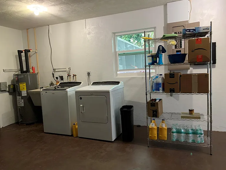 The laundry area next to the garage with washer, drier, a water heater and a shelf full of supplies.