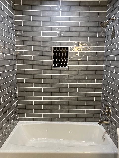 Indulgent tub surround of gray subway tile accented with black hexagon in niche