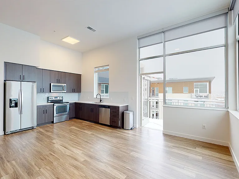 Apartment kitchen with stainless steel appliances, dining and living room with wood-style flooring and balcony or patio.