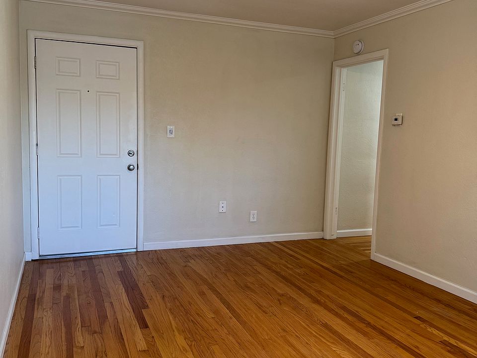 Living room: new ceiling fan, front door on left, hallway to bathroom and bedroom on right. Original hardwood floor.