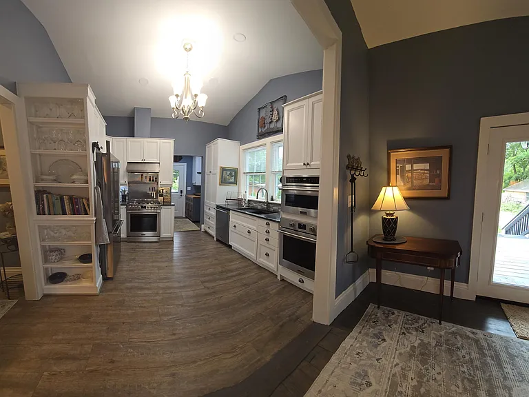 Panoramic view of kitchen with partial keeping room. Dining room table to right expands out to seat 8-10 guests. See view of Laundry/Mud Room and side entrance, off of Kitchen. Note glassware, Bybee serving dishes, cook books in bookcase.