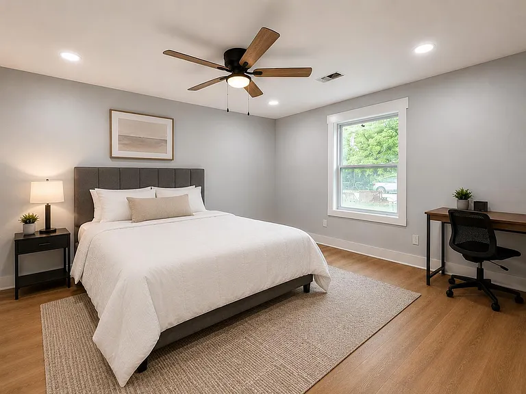 Spacious bedroom with a queen bed, nightstand lighting, ceiling fan, and a dedicated desk area near the window.