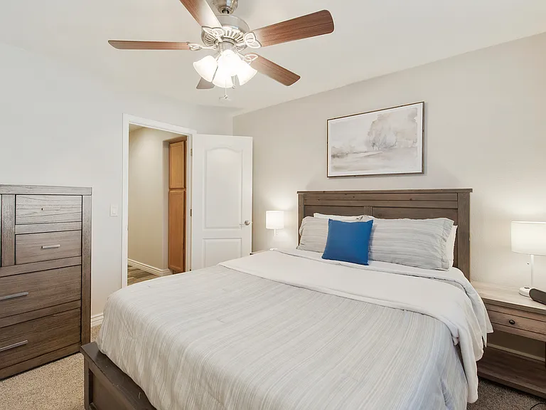 Bedroom 2 features a queen size bed, a dresser, 2 nightstands, a fan and a walk in closet