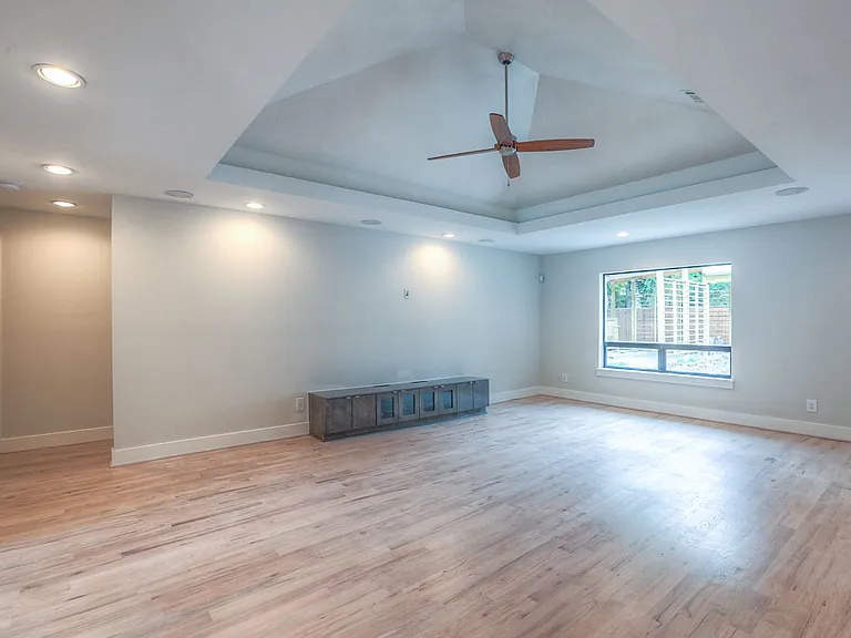Expansive open-concept family room with vaulted-tray ceiling, large window to the side yard, new hardwoods, and built-in media credenza