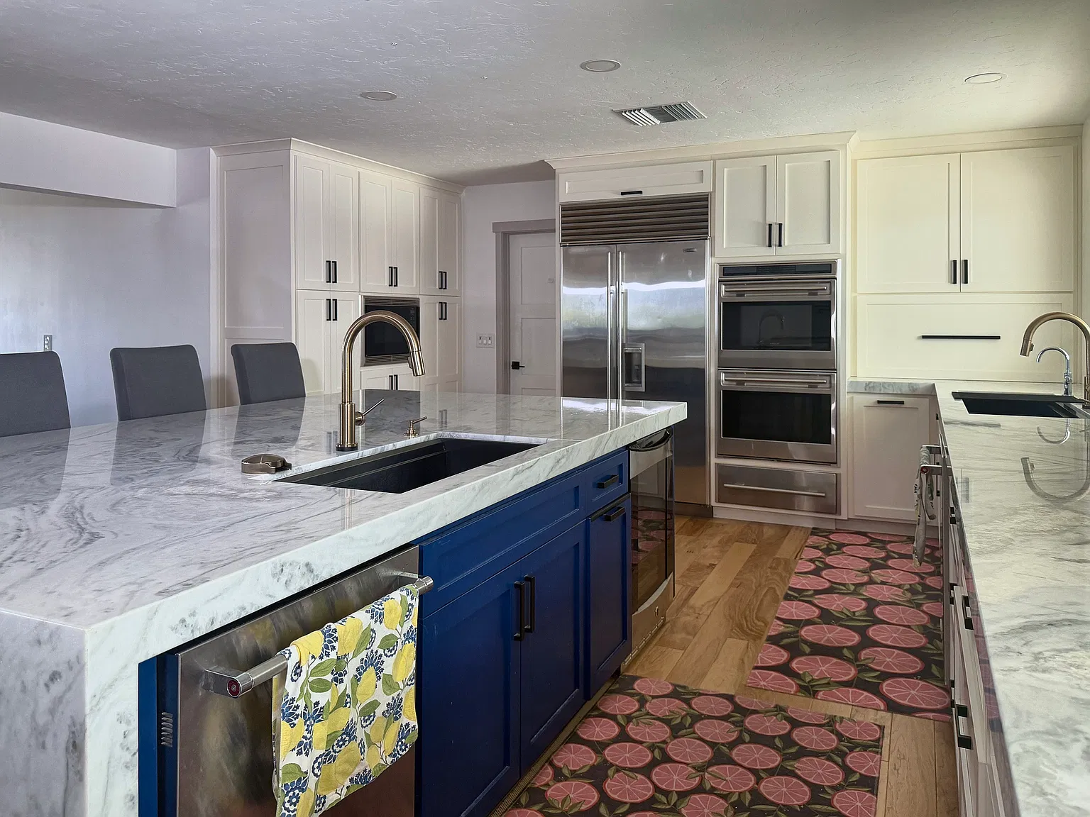Island workstation sinks with touchless faucets, looking toward the Sub-Zero refrigerator and Wolf double oven. Two dishwashers. A beverage fridge. Microwave. Appliance garage. Abundant storage.