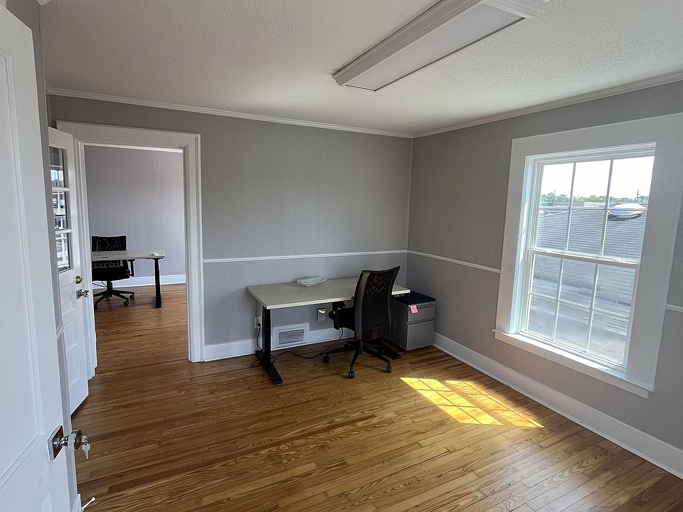 Walking in, the first office has door to hallway, bathroom, second office, and windows on two walls.