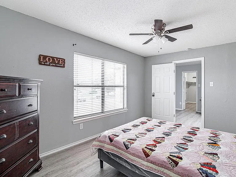 Spacious bedroom with a large window, ceiling fan, and wood-style flooring, with easy access to the hall and closet.