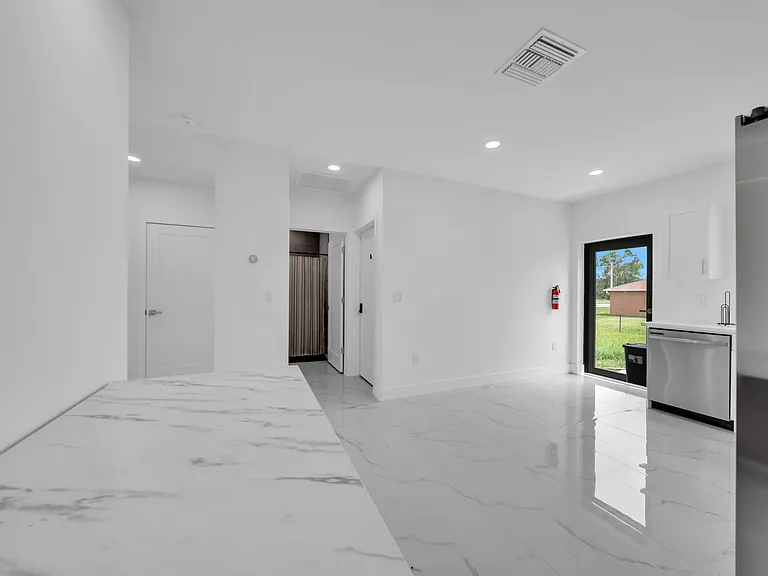 Open kitchen area with marble-look flooring, recessed lighting, stainless dishwasher, and a door leading to the yard.