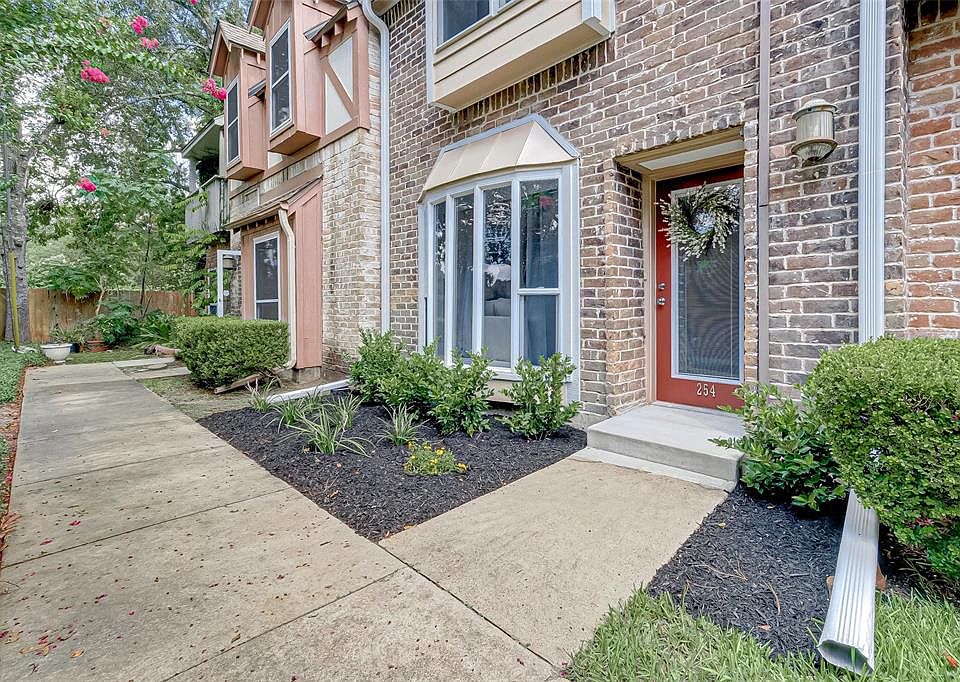 The front facade of Unit 254 has a red front door with built in blinds and a bay window looking out at beautiful landscaping.