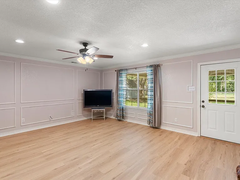 Spacious room featuring light wood-finish flooring, decorative wall molding, a ceiling fan with integrated lighting, recessed ceiling lights, and a white paneled door with a multi-pane glass insert