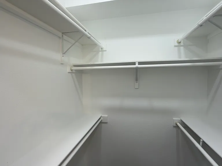 Walk-in closet featuring white walls, integrated shelving, and multiple hanging rods for organization.