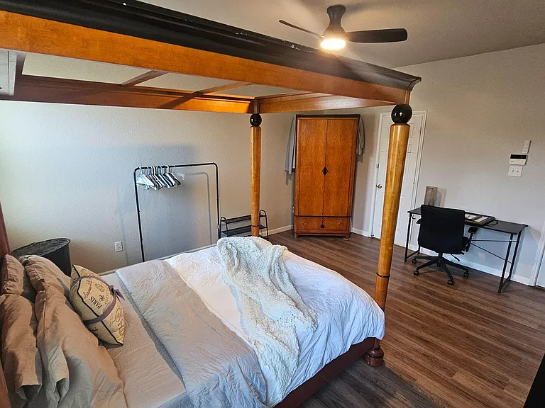 Spacious furnished bedroom with a four-poster bed, wood-look floors, wardrobe storage, and a dedicated desk workspace.
