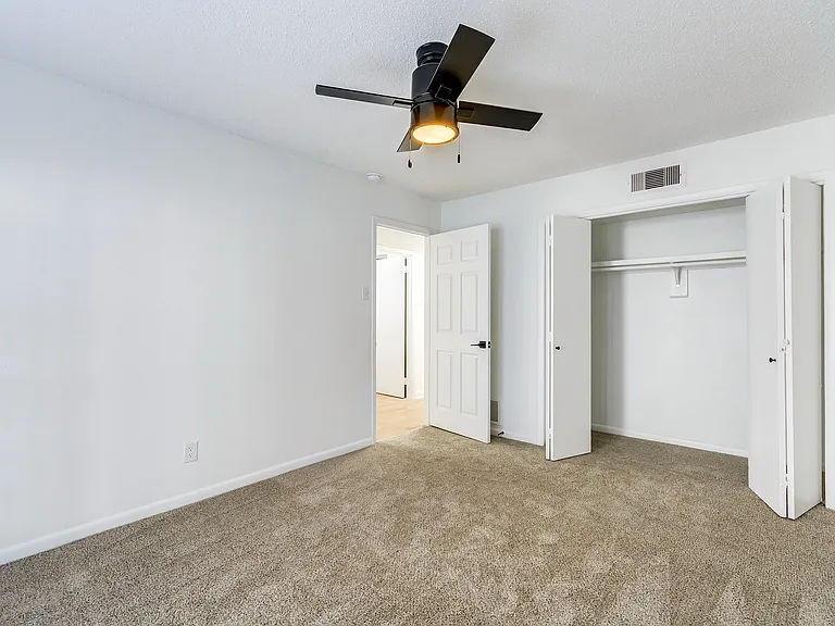 A carpeted bedroom with oversized closet and ceiling fan is shown at ReNew on Cantrell.