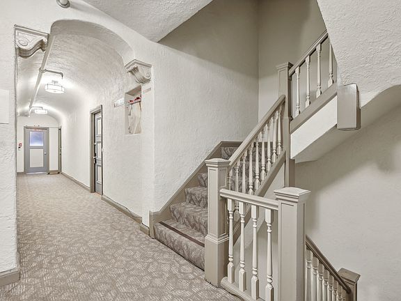 Hallway with a carpet, set of stairs with a railing and banister