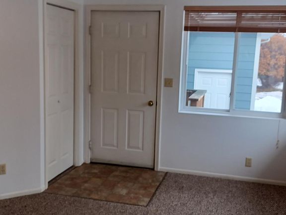 Living room view of front door. New paint and new carpet. ceiling fan.