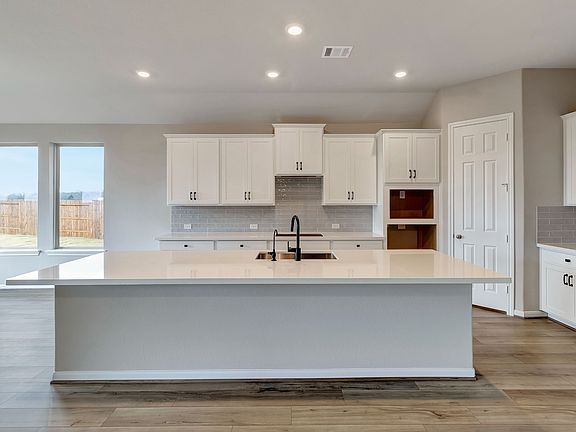 The spacious kitchen features white cabinets, quartz countertops and a modern tile backsplash. Larg