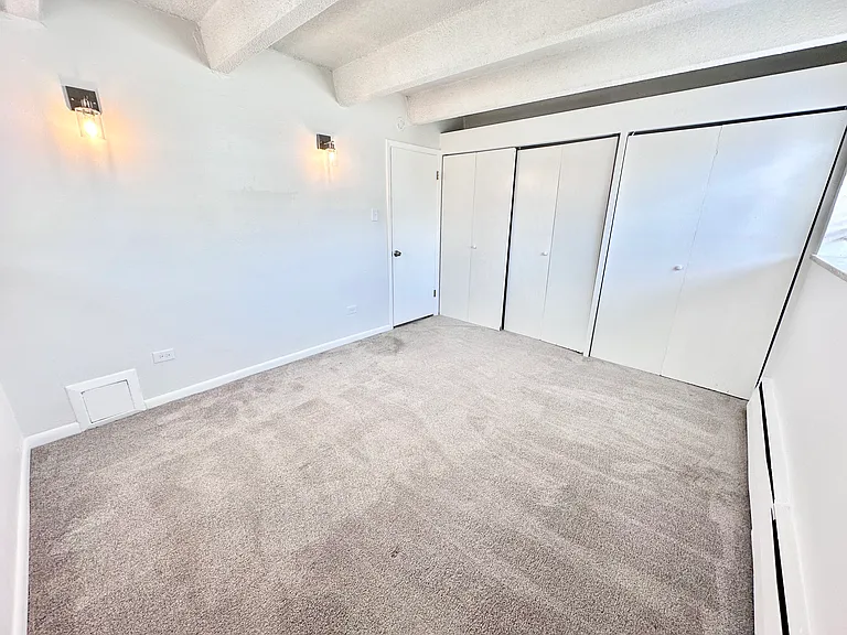 Bright room with plush carpeting featuring modern wall lighting and ample closet space. Bright room with plush carpeting featuring modern wall lighting and ample closet space.