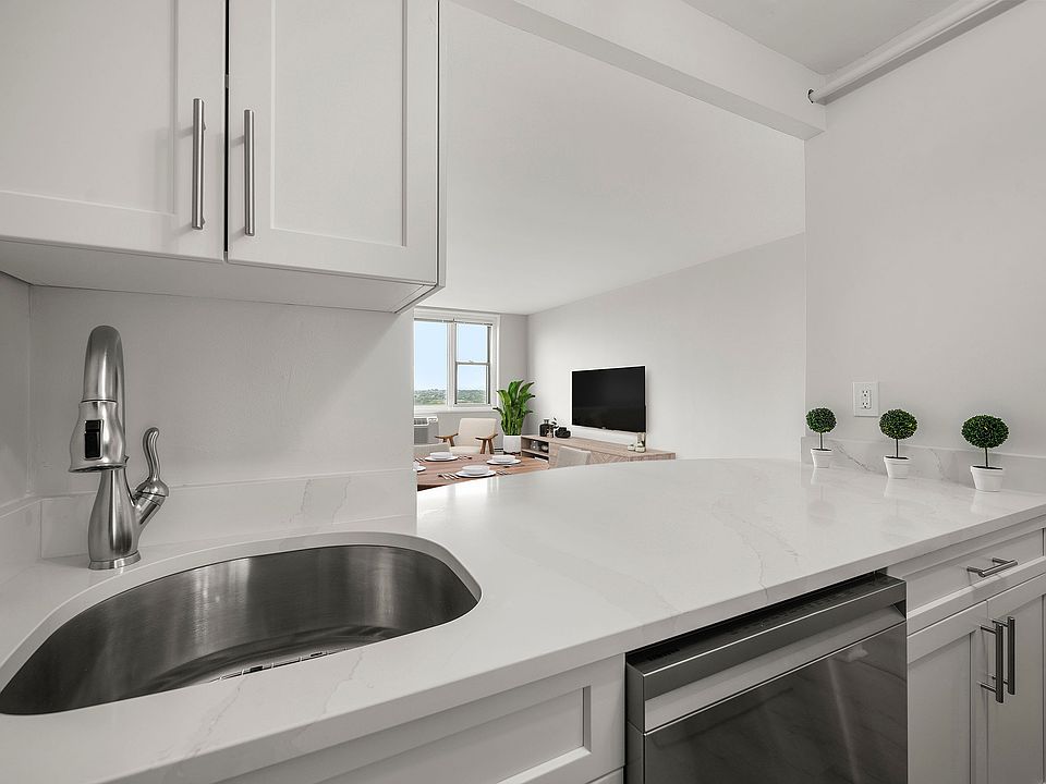Modern kitchen with sleek stainless-steel appliances, statuario quartz countertops, and six burner gas stove, opening into a bright living area with a large window view at Parkside Place, apartments in Cambridge, MA