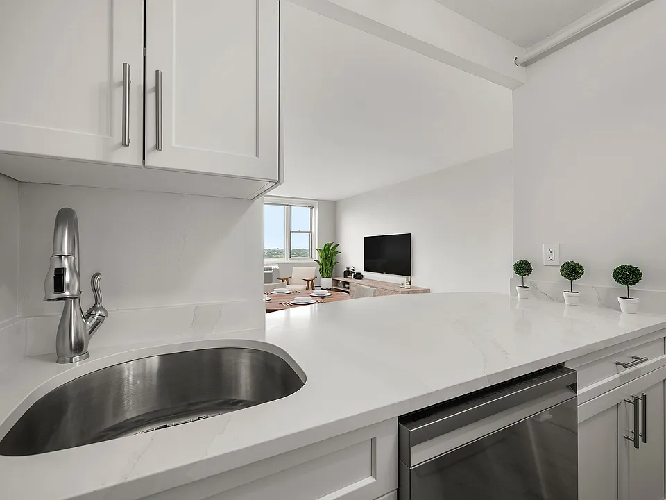 Modern kitchen with sleek stainless-steel appliances, statuario quartz countertops, and six burner gas stove, opening into a bright living area with a large window view at Parkside Place, apartments in Cambridge, MA