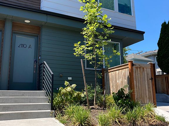 Small front yard with trashcans hidden in wooden enclosure.
