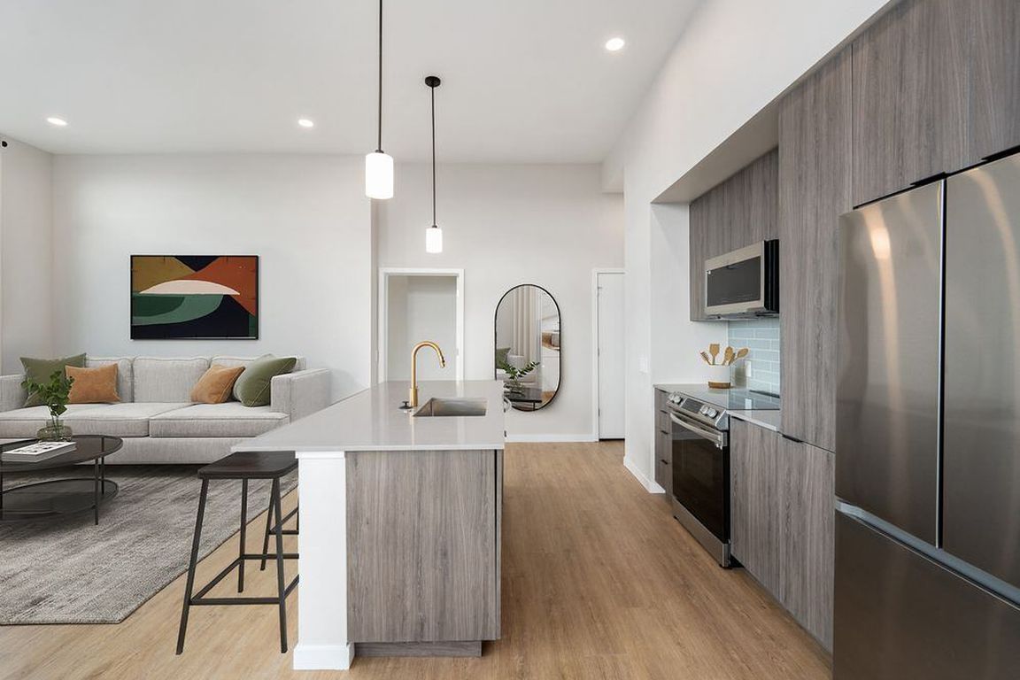 Signature Collection kitchen with dark cabinetry, marbled quartz countertops and backsplash, upgraded stainless steel appliances, and pendant lighting.