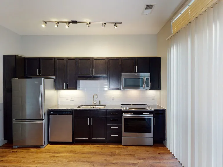 Apartment kitchen with stainless steel appliances, granite countertops and wood-style flooring.